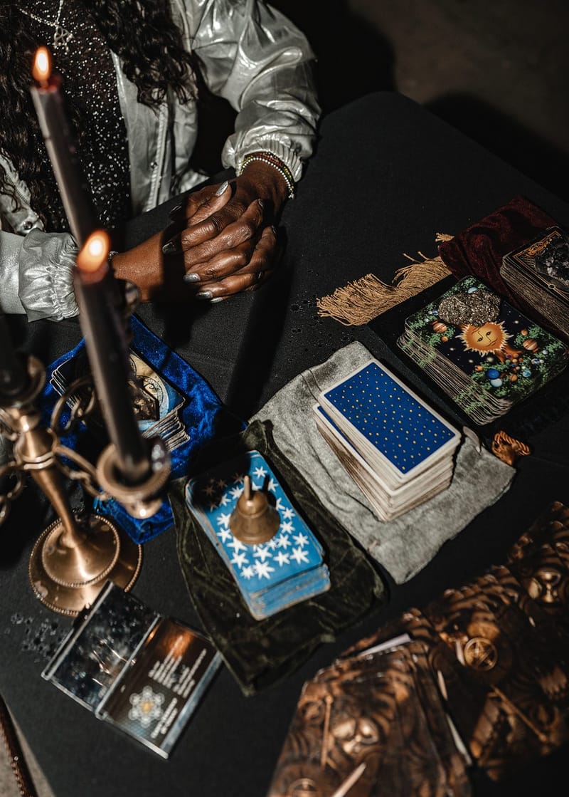 Tarot decks, velvet pouches and a lit black taper candle in a brass holder on a black table