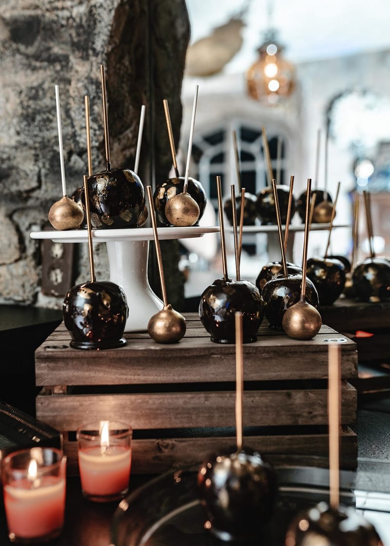 Black and gold candy apples on sticks on a white cake stand set on a wooden crate with candles