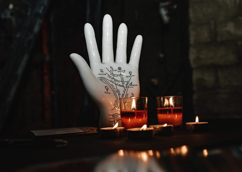 White palmistry hand sculpture with red votive candles and tea lights on a dark table