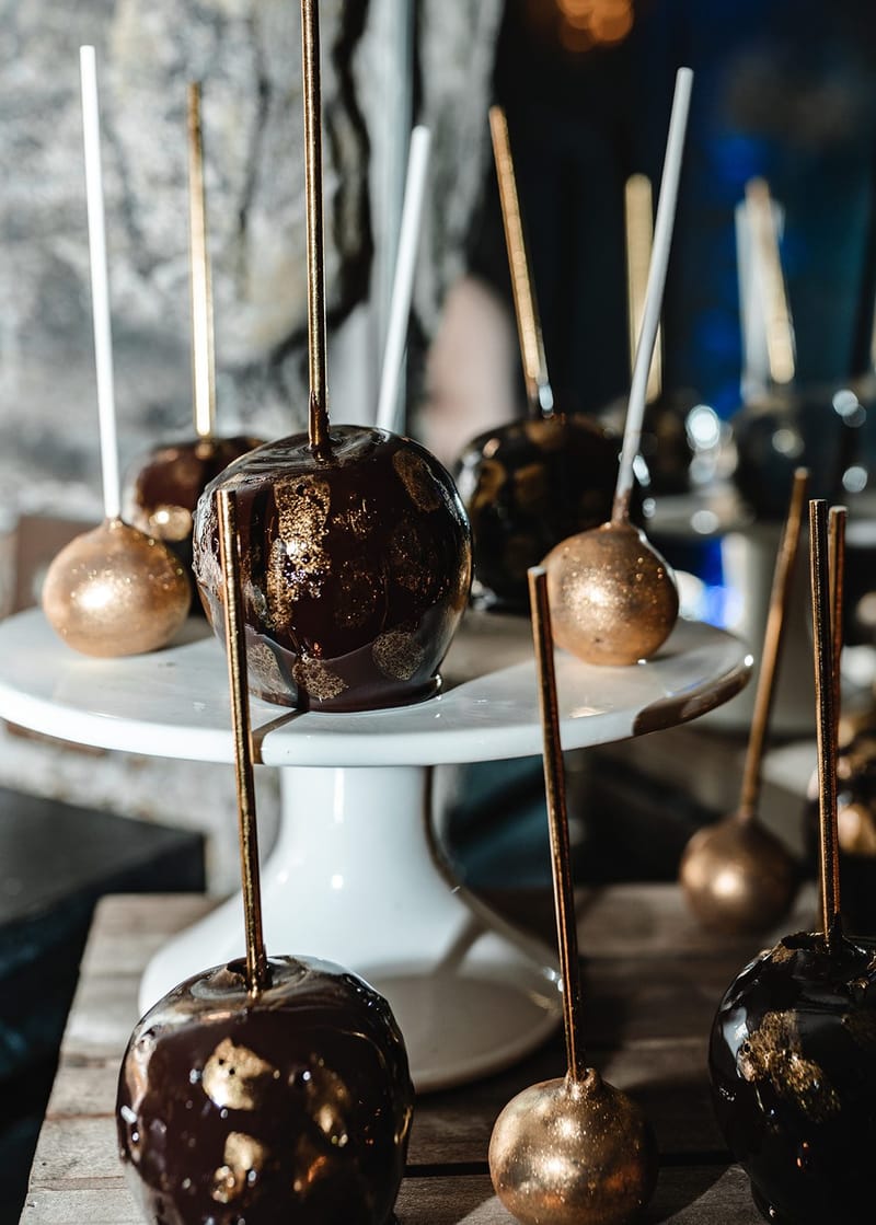 Close-up of black candy apples flecked with gold beside gold spheres on sticks