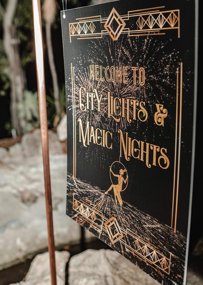 Art deco sign reading Welcome to City Lights & Magic Nights over a gold fireworks design