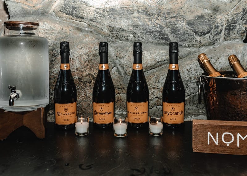 Champagne bottles labelled Carbon6, Wayflyer, Viscap Media and unybrands with votive candles and an ice bucket