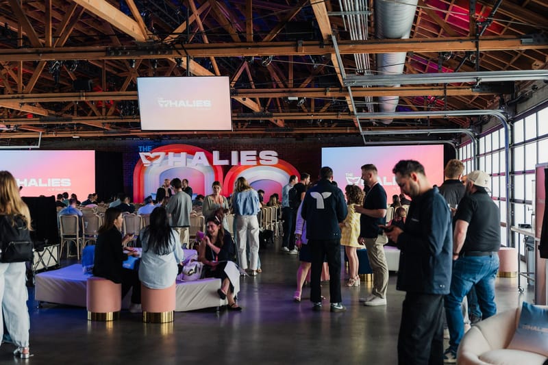 Guests mingling in a hall with pink ottomans, Whalies screens and the main stage at the far end