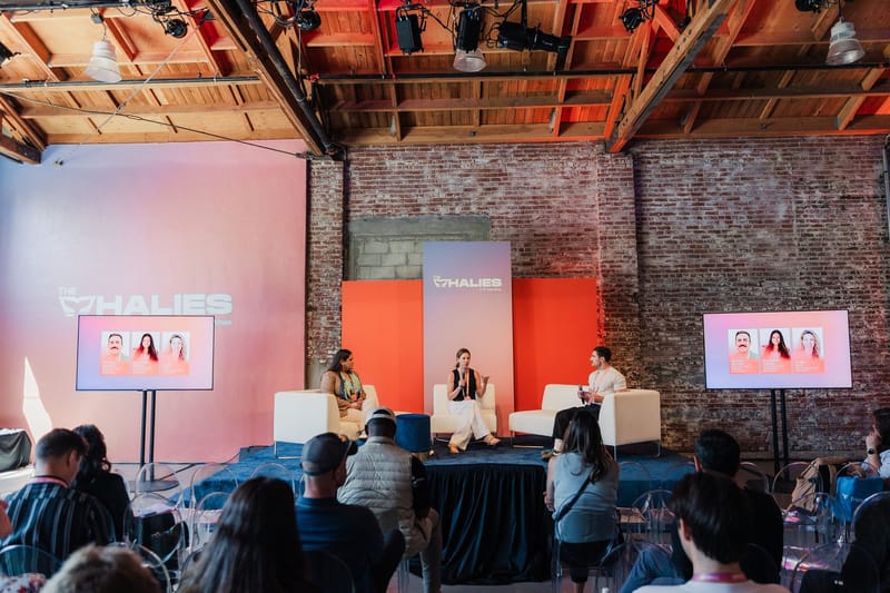 Three speakers on white chairs between two screens in a brick room with a Whalies backdrop