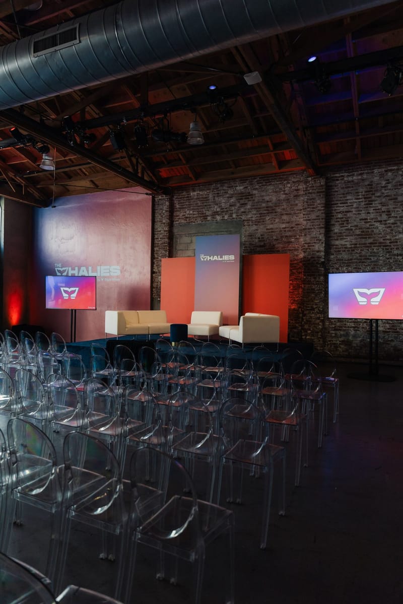 Rows of clear chairs facing a small stage with white sofas and Whalies screens