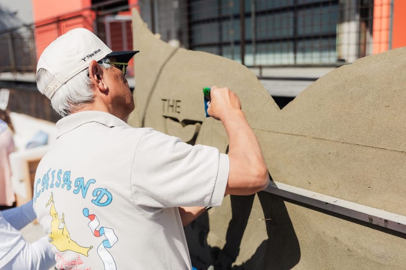 Sculptor in a Triple Whale cap carving lettering into a sand sculpture
