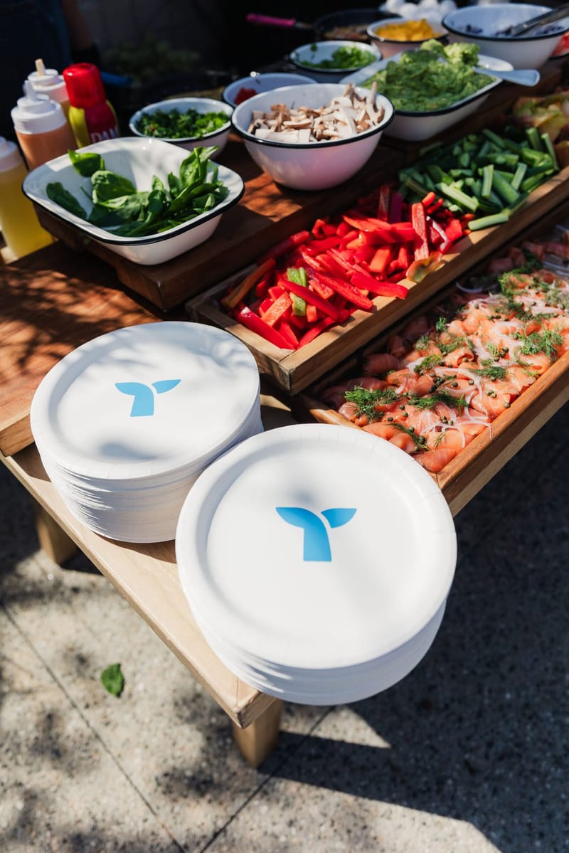 Salad bar with sliced red peppers, greens and stacks of plates printed with the Triple Whale logo