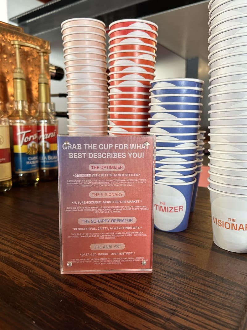 Sign reading Grab the cup for what best describes you! beside cups labeled The Optimizer and The Visionary