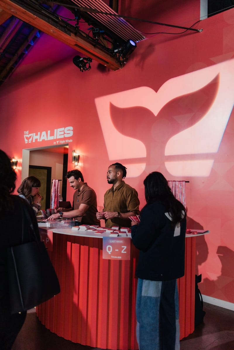 Staff at a curved red check-in counter with a Last Name Q-Z sign and a projected whale tail