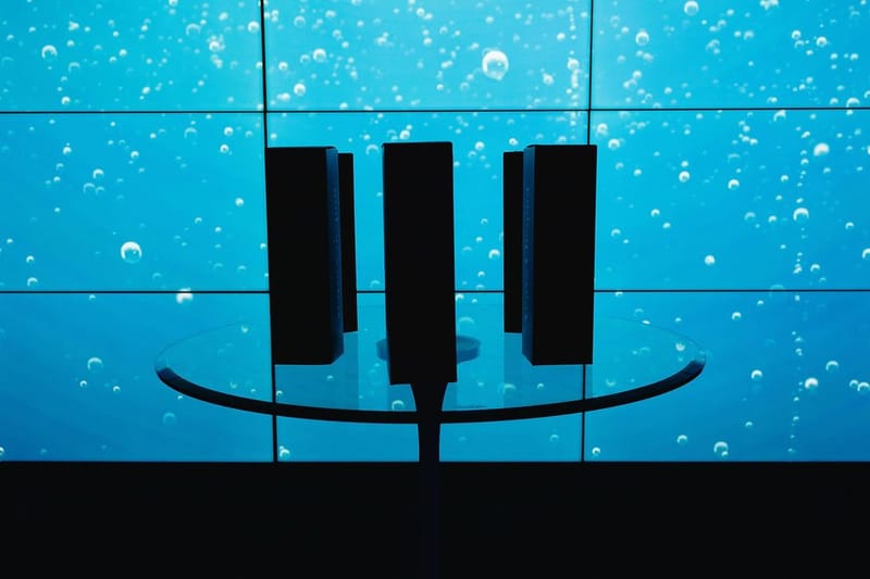 Round glass table in silhouette against a video wall of blue water and bubbles
