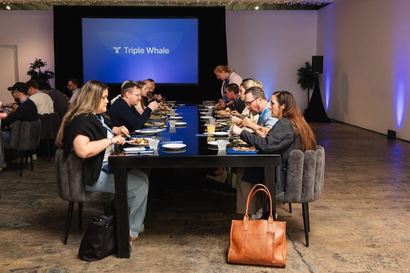 Guests eating lunch at a long black table in front of the Triple Whale screen