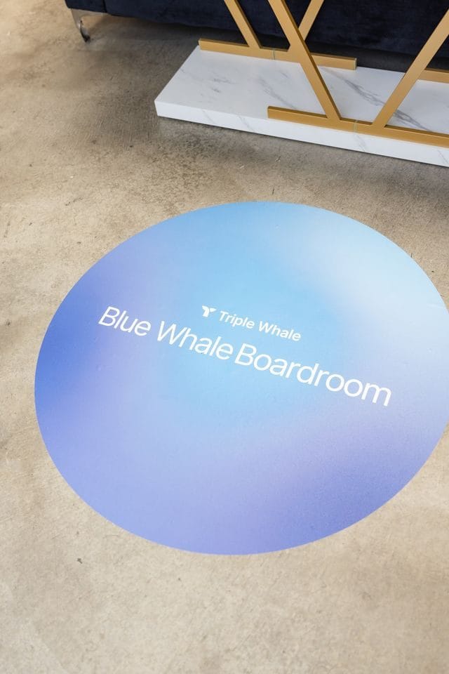 Close view of a round blue floor decal reading Triple Whale Blue Whale Boardroom