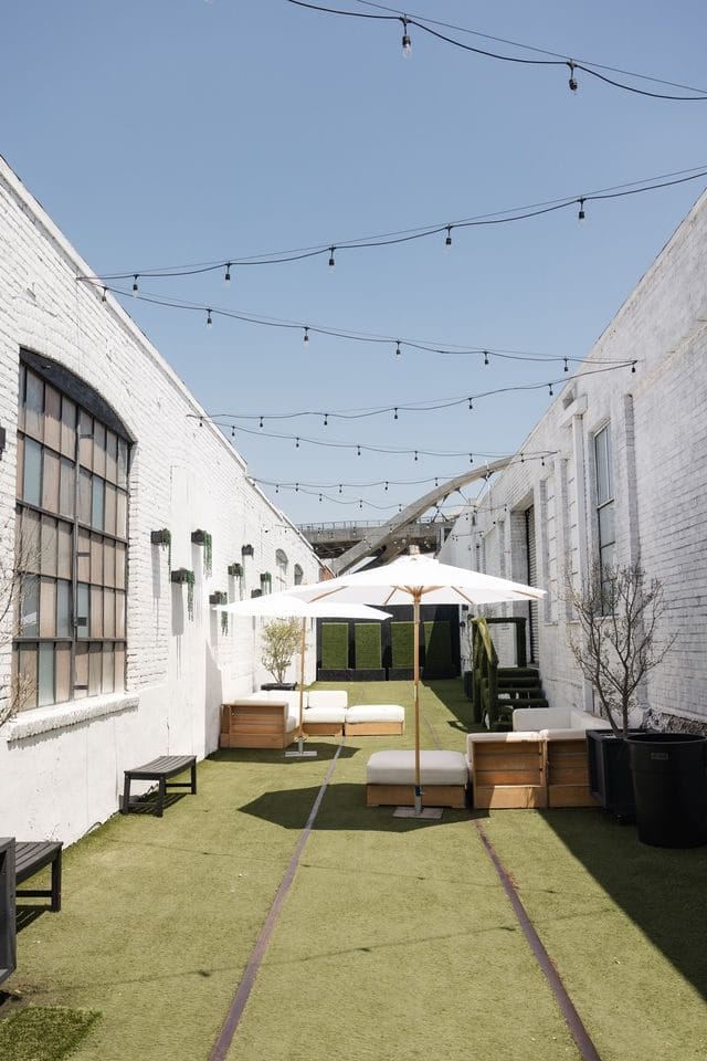 Outdoor courtyard with artificial turf, white umbrellas and lounge seating under string lights