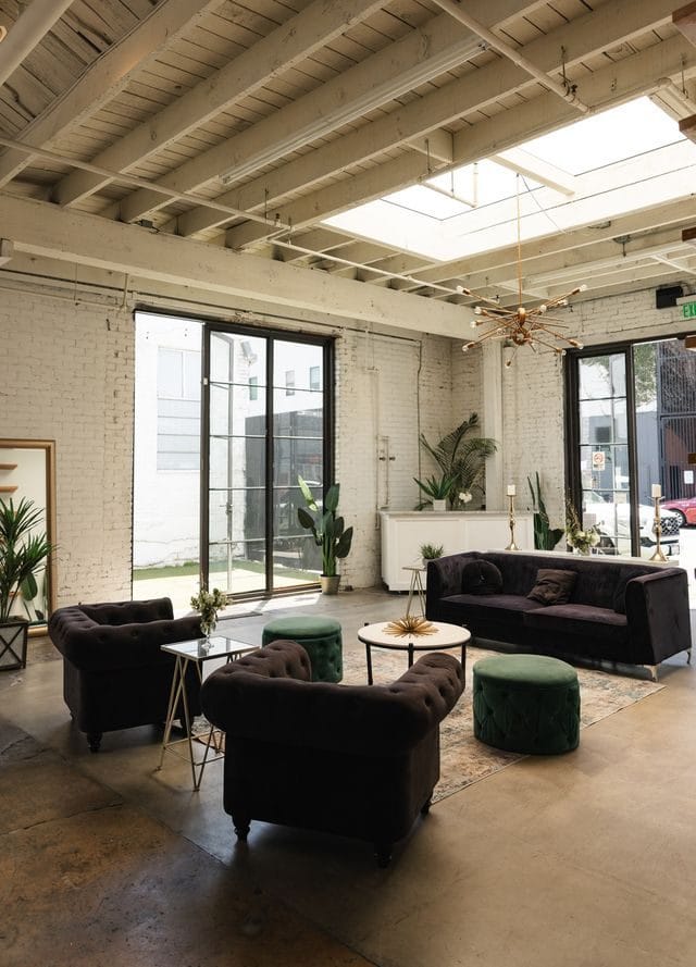 Lounge with black tufted sofas, green ottomans and potted plants beneath a skylight