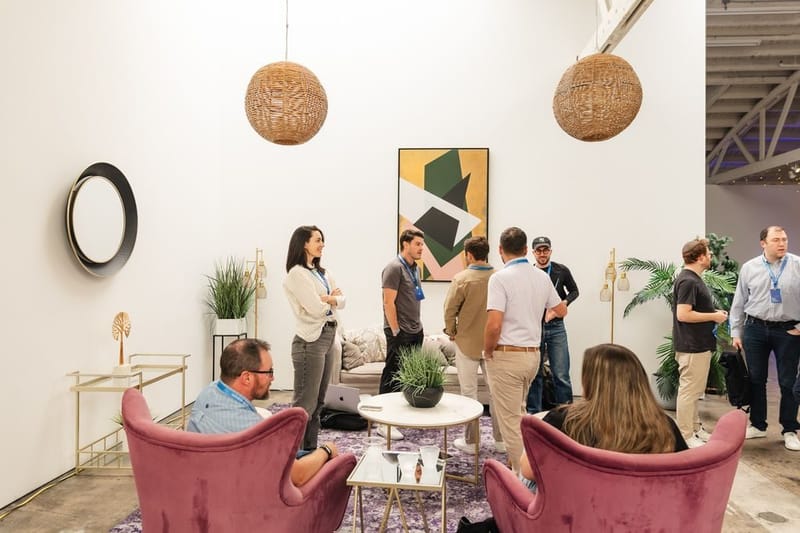 Guests talking in a lounge with pink velvet armchairs and woven pendant lights