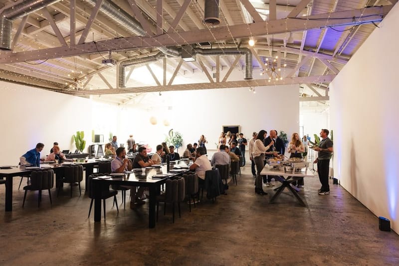 Guests mingling around the long tables and buffet in a white room with exposed trusses