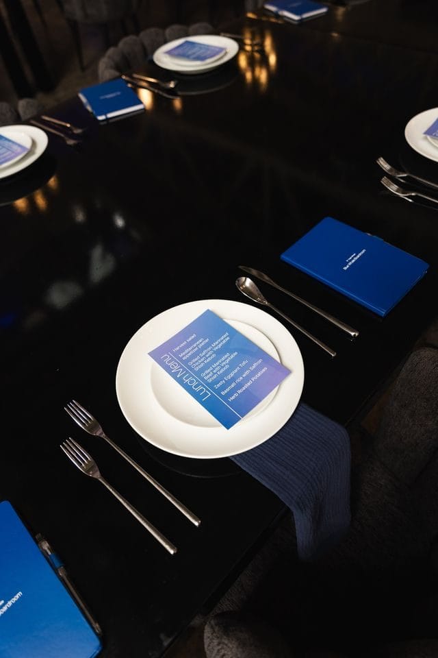 Black table place setting with a Lunch Menu card on a white plate, navy napkin and blue notebook