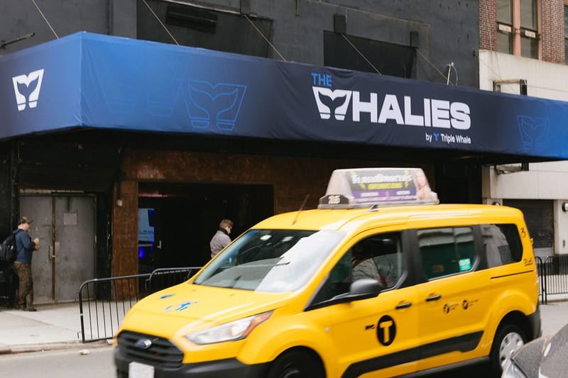 Navy awning printed THE WHALIES by Triple Whale above the venue doors, with a yellow taxi passing