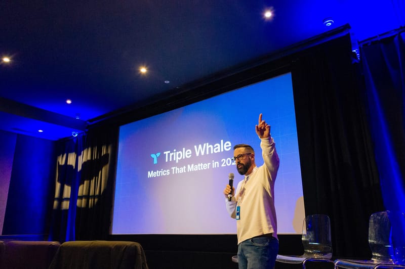 Speaker pointing upward in front of a screen reading Triple Whale Metrics That Matter