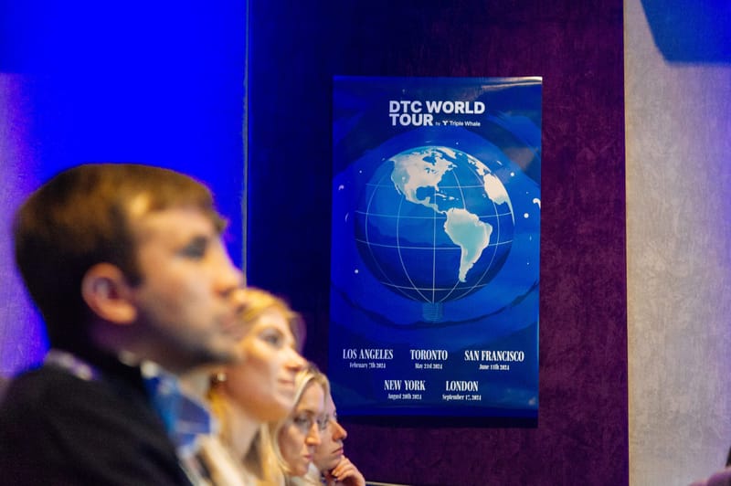 Guests listening beside a DTC World Tour poster listing dates for Los Angeles, Toronto, San Francisco, New York and London