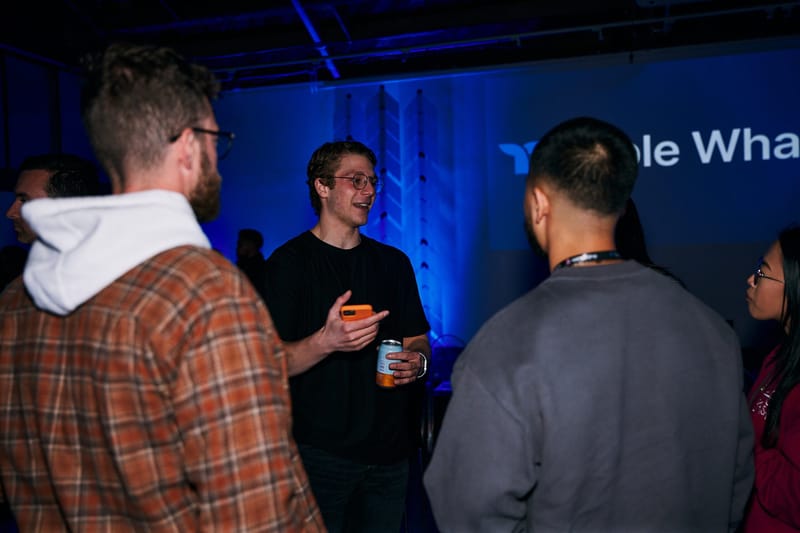 Guests talking in a small group in front of blue-lit Triple Whale lettering and a chevron column