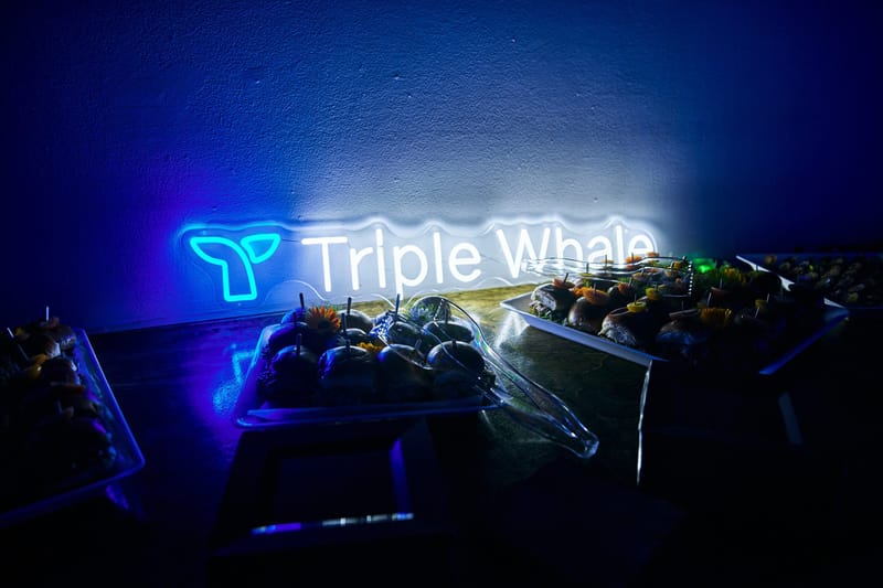 Neon Triple Whale sign glowing behind trays of sliders garnished with small flowers