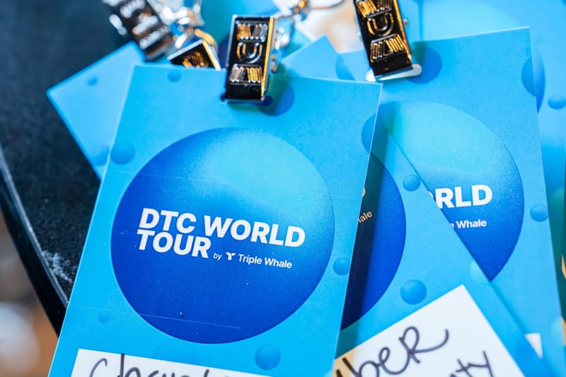 Light blue DTC World Tour by Triple Whale badges with metal clips and handwritten name labels
