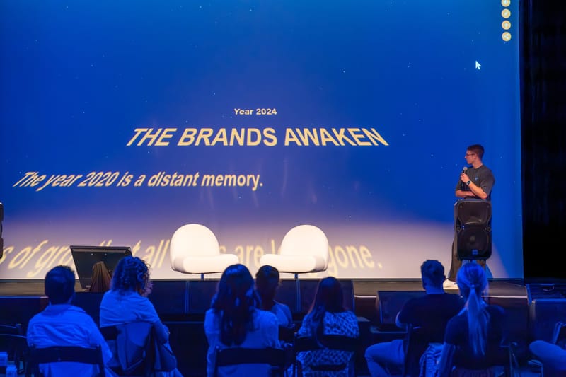 Speaker with a microphone beside a slide reading Year 2024, The Brands Awaken, The year 2020 is a distant memory