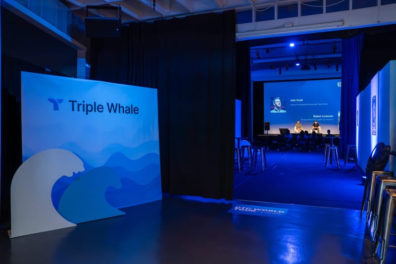 Triple Whale backdrop with wave cutouts beside a curtained doorway looking through to a panel on stage
