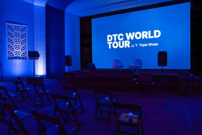 Empty seminar room with a DTC World Tour screen, folding chairs and a carved lattice wall panel lit blue