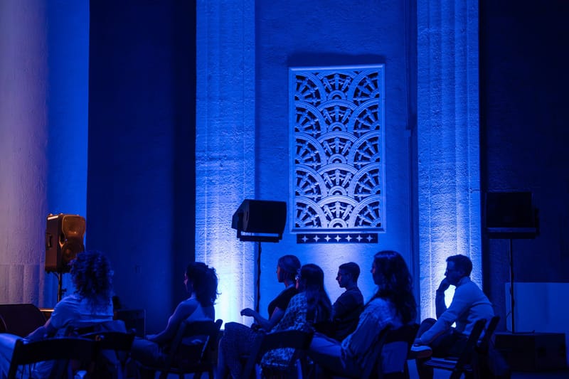 Guests in silhouette seated beneath a carved fan-pattern lattice panel lit blue