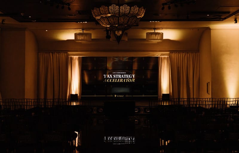 Empty ballroom with a chandelier and rows of chairs facing a Tax Strategy Accelerator screen