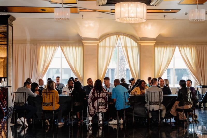 Attendees seated around tables in a bright room with arched windows and chandeliers