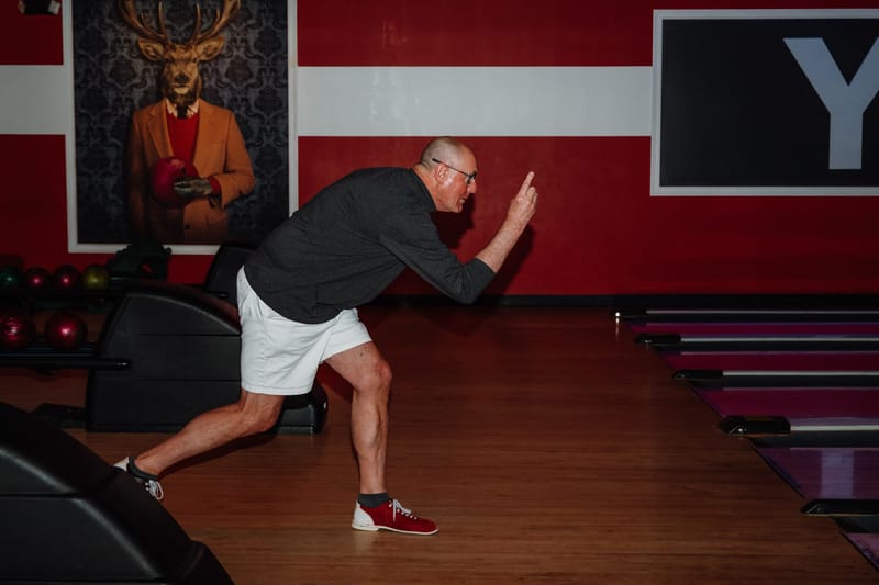 A man bowling in front of a wall with a painted stag portrait and red stripes