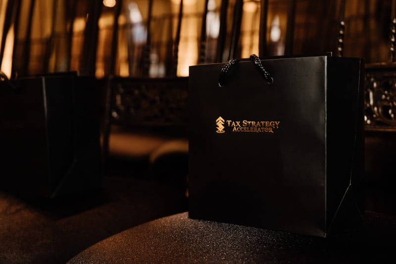 Black gift bag printed with the gold Tax Strategy Accelerator logo