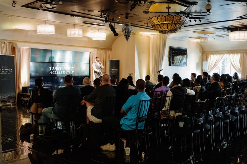 Seated audience listening to a speaker beside screens in a cream ballroom