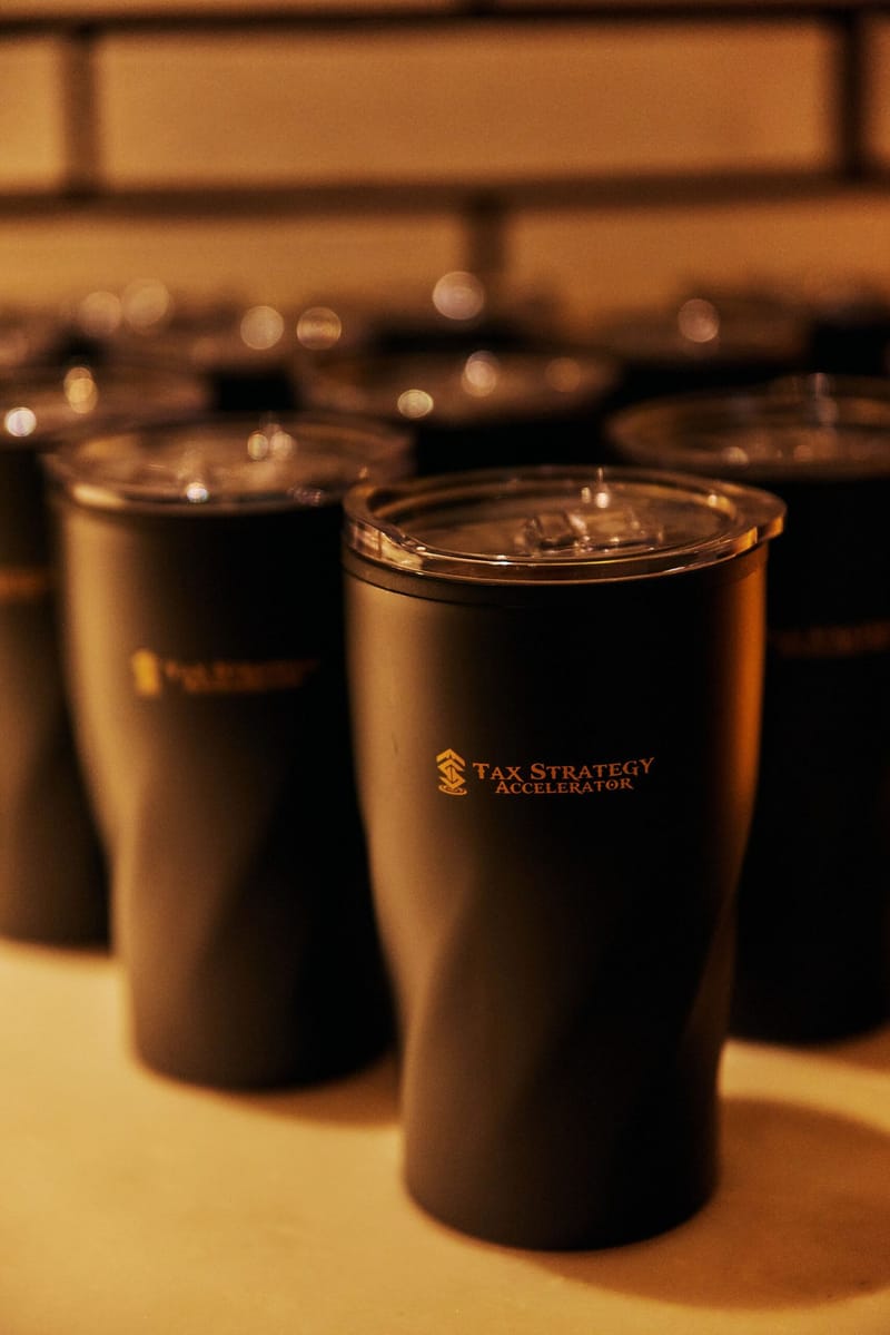 Black tumblers with clear lids printed with the gold Tax Strategy Accelerator logo
