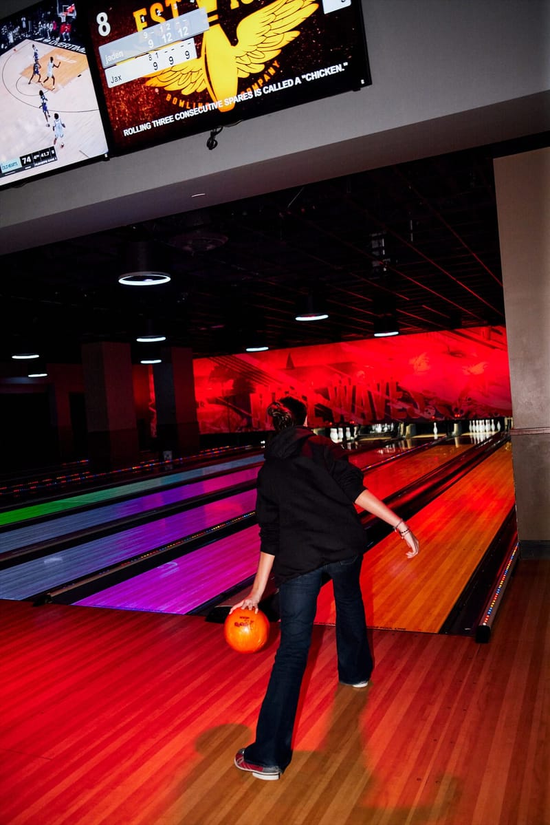 A guest bowling on a lane lit in red and purple under scoreboard screens