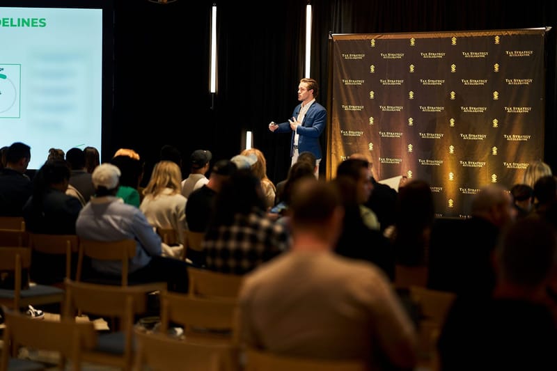 Seated audience facing a speaker and a green and white presentation slide