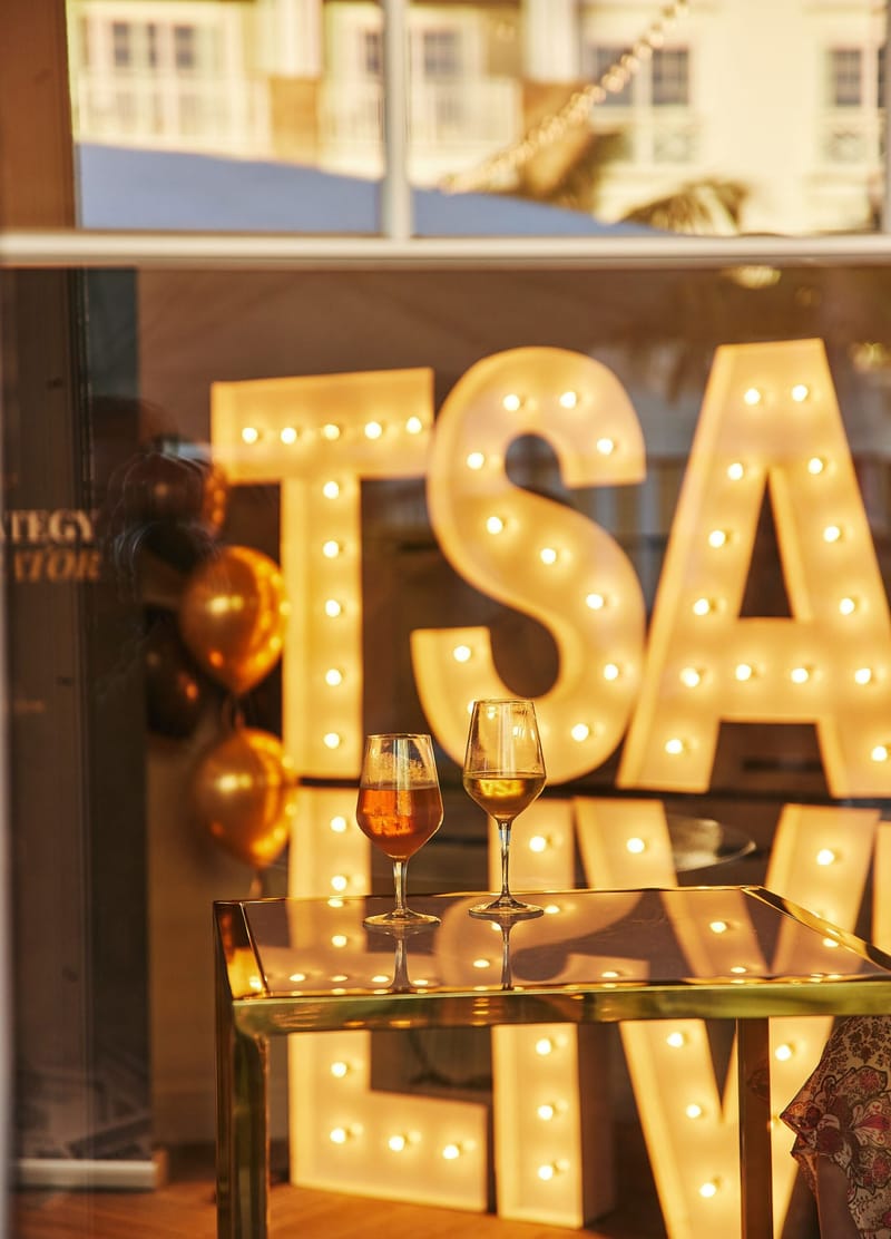 TSA LIVE marquee letters and gold balloons behind two glasses of wine on a gold table