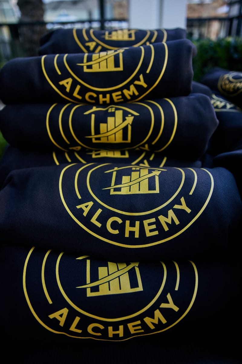 Stack of folded navy sweatshirts printed with the gold Tax Alchemy logo