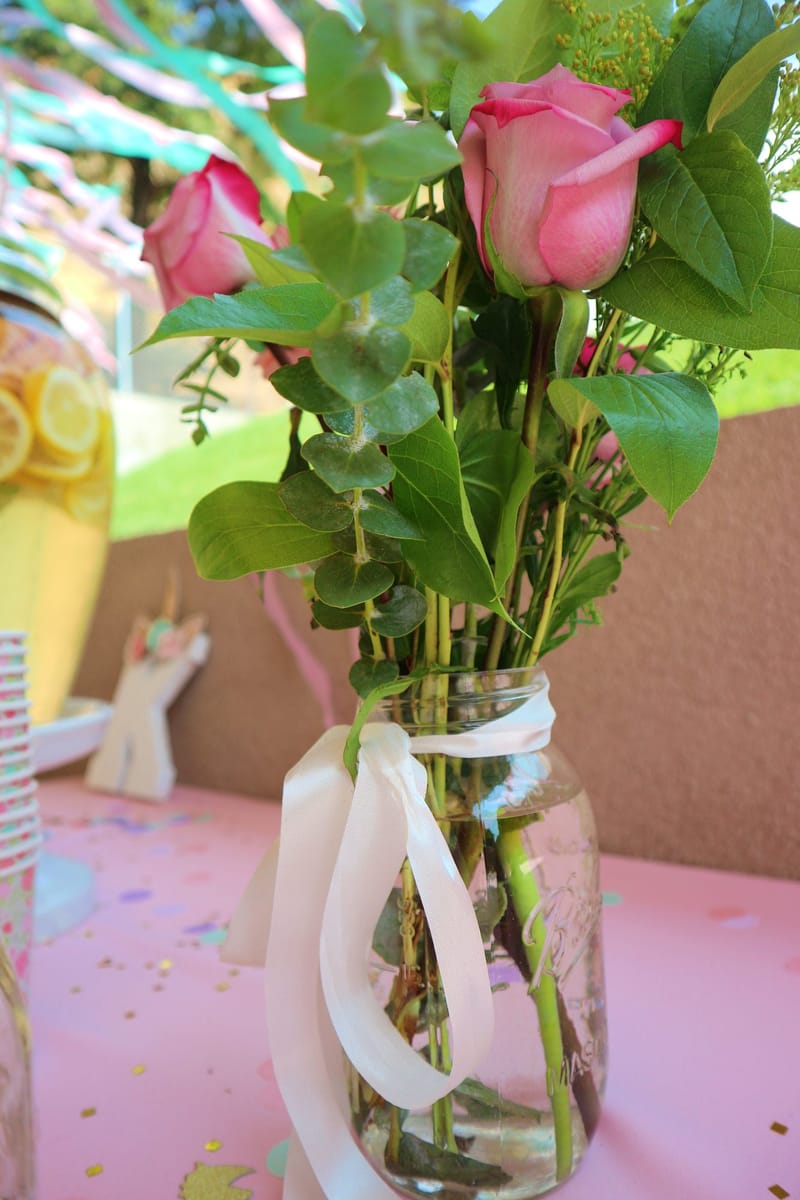 Pink roses and eucalyptus in a glass jar tied with a white ribbon on a pink tablecloth