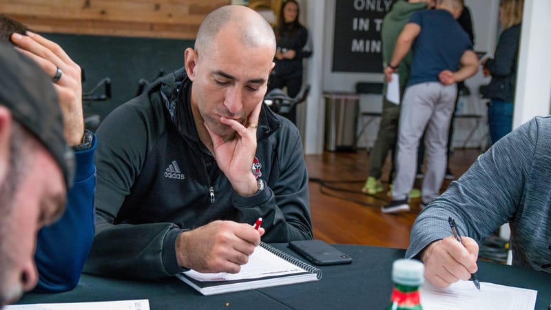 An attendee in a black jacket thinking over his open notebook, pen in hand, at a black table