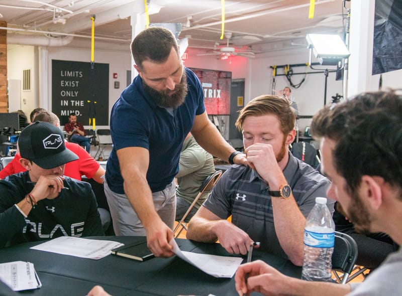 The presenter leaning over attendees' notes at a table, under a sign reading Limits exist only in the mind