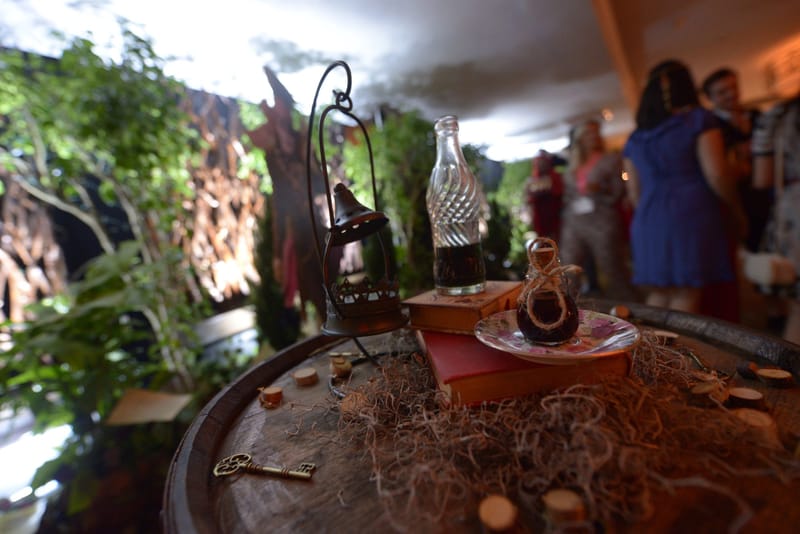 Wooden barrel topped with a hanging lantern, a glass bottle, old books and a key, guests talking behind