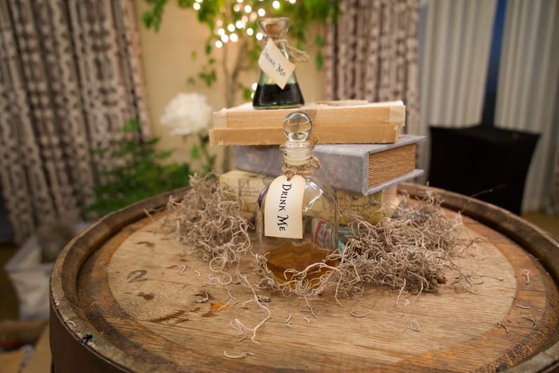 Two Drink Me bottles on a stack of old books in dried moss on top of a wooden barrel