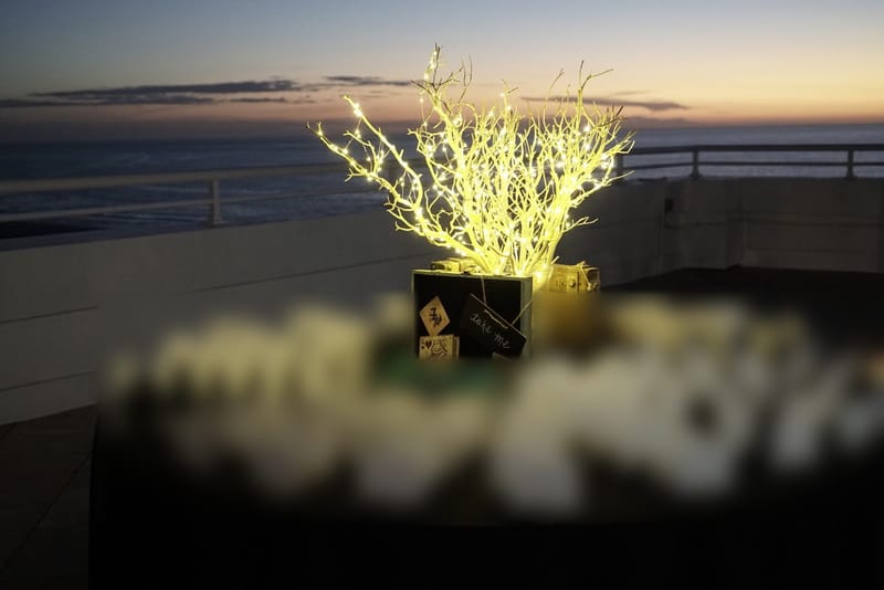 Round table of name badges and green lanyards around a lit white branch centerpiece, the sea at sunset behind