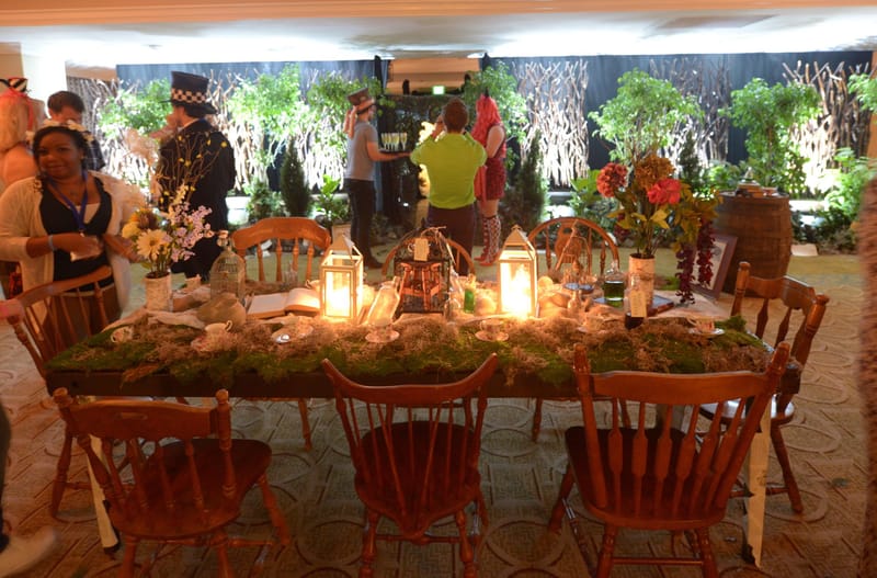 Long table with a moss runner, lit lanterns and flowers, guests gathered around it under a canopy