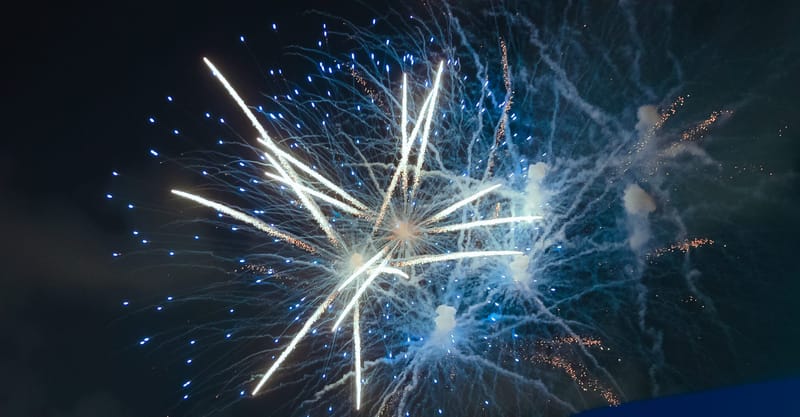 White and blue fireworks bursting against a dark night sky
