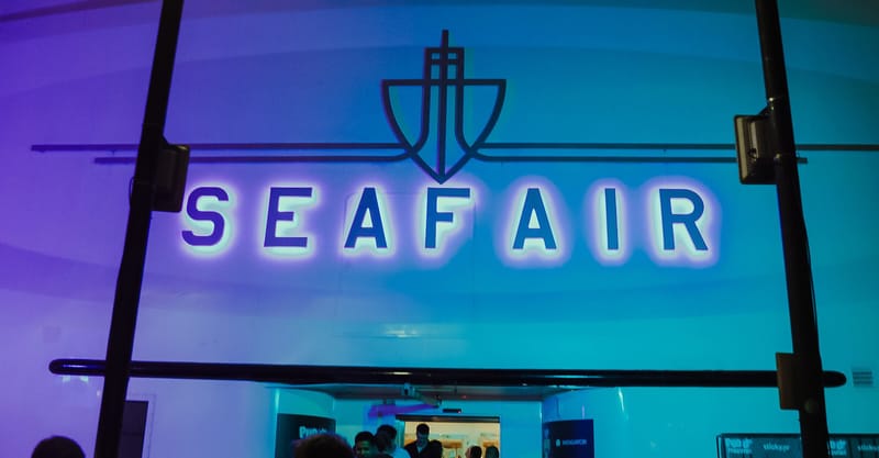 Lit SEAFAIR lettering and anchor logo above glass doors in blue and purple light